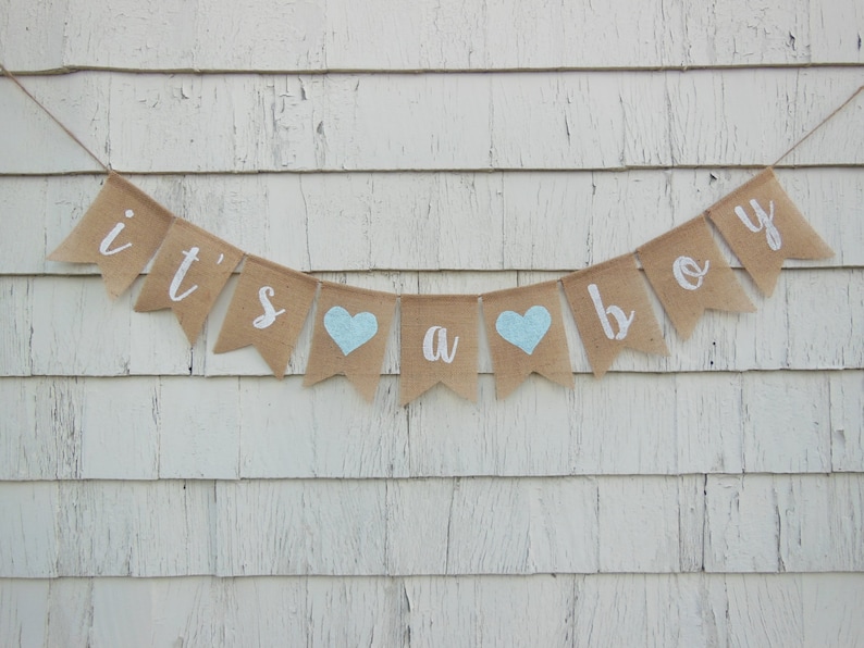 May include: A burlap banner with the words "it's a boy" in white lettering. The banner has two light blue hearts.