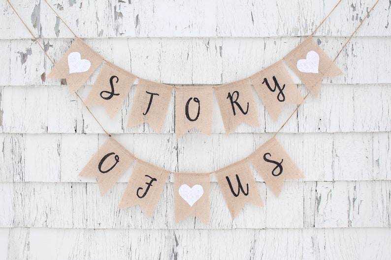 May include: A burlap banner with the words "STORY OF US" in black lettering. The banner is strung with twine and has white felt hearts between each letter.