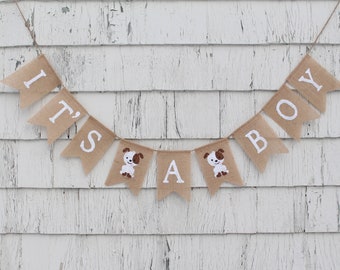 Może przedstawiać: Baner z juty z napisem "It's a Boy" białymi literami. Baner jest ozdobiony małymi, białymi ilustracjami psów.
