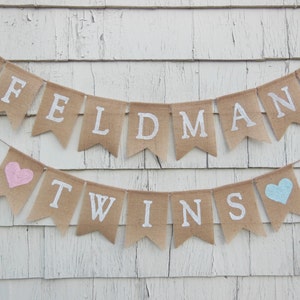 May include: A burlap banner with the text "Feldman Twins" in white paint. The banner is decorated with pink and blue hearts.