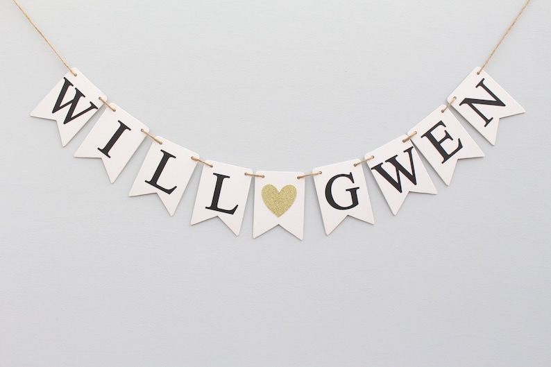 May include: White banner with black letters spelling "WILL" and "GWEN" with a gold glitter heart in between.