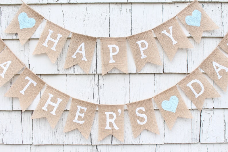 May include: A burlap banner with the words "Happy Father's Day" in white paint. The banner has three blue hearts.