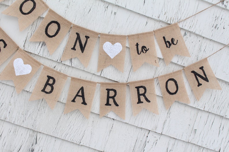 May include: A burlap banner with the text "Soon to be Barron" in black lettering. The banner has two white hearts and is strung with twine.