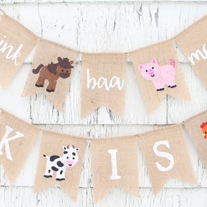 Pu&ograve; includere: Un banner di iuta con testo bianco e illustrazioni di animali della fattoria. Il banner include le parole "oink", "baa" e "moo", insieme a immagini di un cavallo, un maiale, una mucca e un gallo. Il banner &egrave; infilato su uno spago.