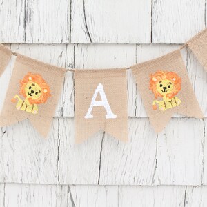 May include: A burlap banner with the letters "S A B" in white paint. Each letter is on a separate flag with a small orange lion illustration.