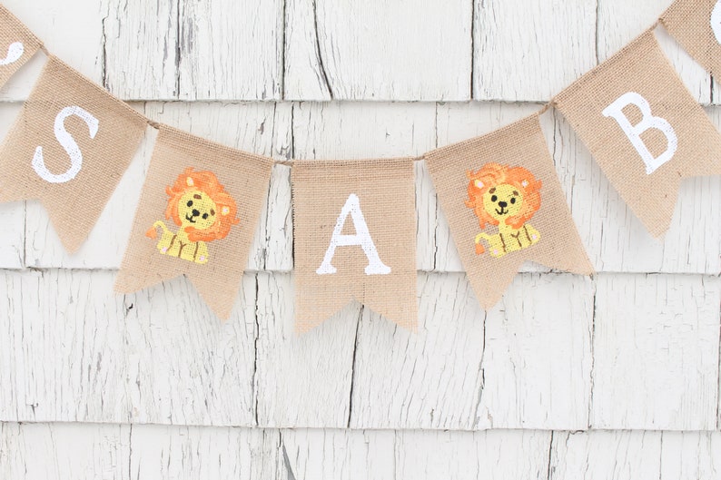 May include: A burlap banner with the letters "S A B" in white paint. Each letter is on a separate flag with a small orange lion illustration.