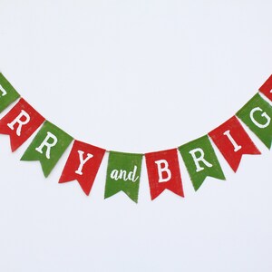 May include: A festive banner with red and green pennants spelling "MERRY and BRIGHT" in white letters. The banner is strung on a thin brown string, perfect for holiday decorations. The background is plain white.