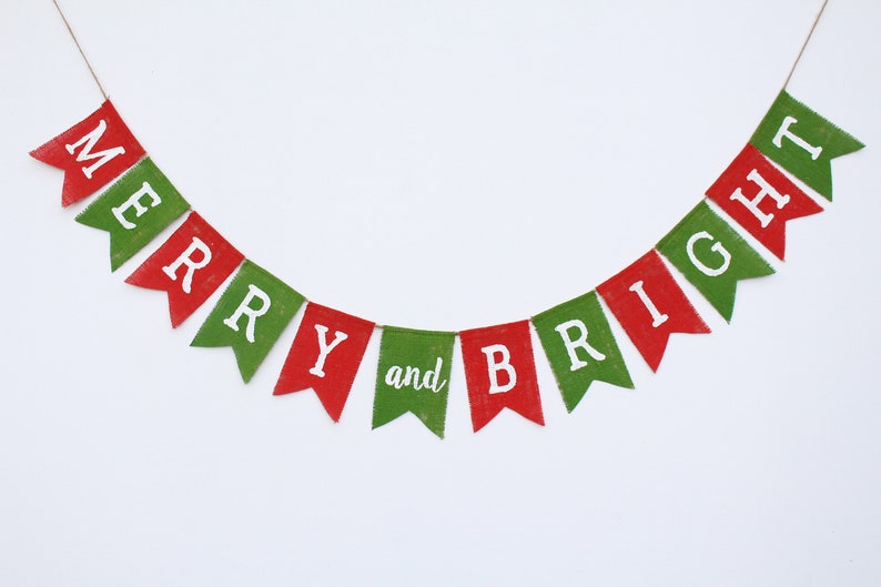 May include: A festive banner with red and green pennants spelling "MERRY and BRIGHT" in white letters. The banner is strung on a thin brown string, perfect for holiday decorations. The background is plain white.