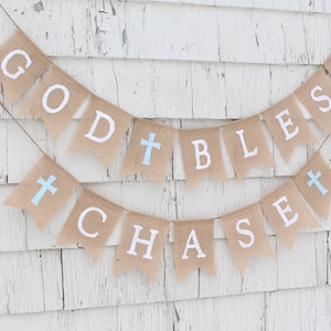 May include: A burlap banner with the words "God Bless Chase" in white letters. The banner has blue crosses between each word.