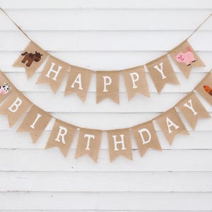 May include: A burlap banner with the words "Happy Birthday" in white letters. The banner is decorated with farm animal illustrations, including a cow, pig, horse, and rooster.