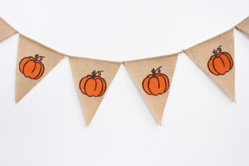 May include: A bunting banner made of burlap, featuring orange pumpkin designs. Each triangular flag displays an orange pumpkin with a brown stem. Ideal for autumn or Halloween decorations, strung with twine.