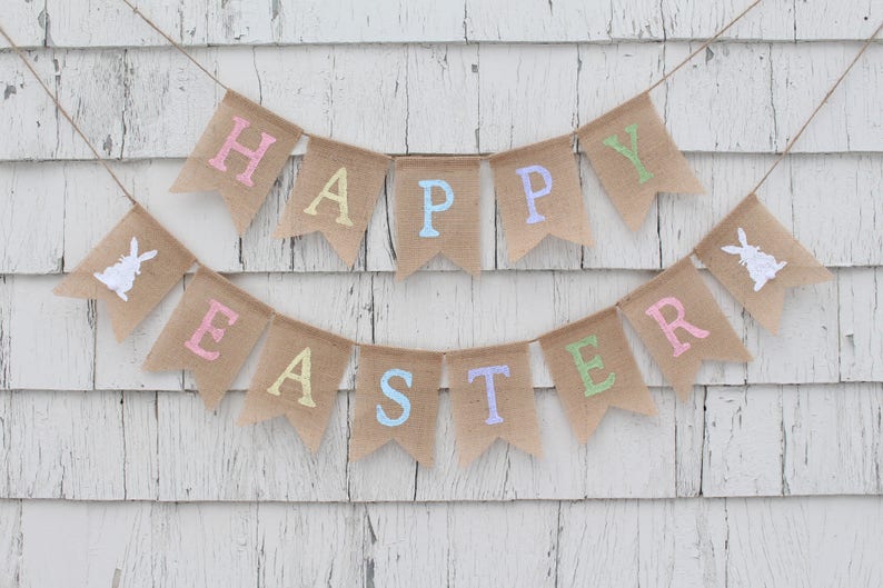 May include: A burlap banner with the words "Happy Easter" in pastel colors. The banner is strung on a white wooden wall.