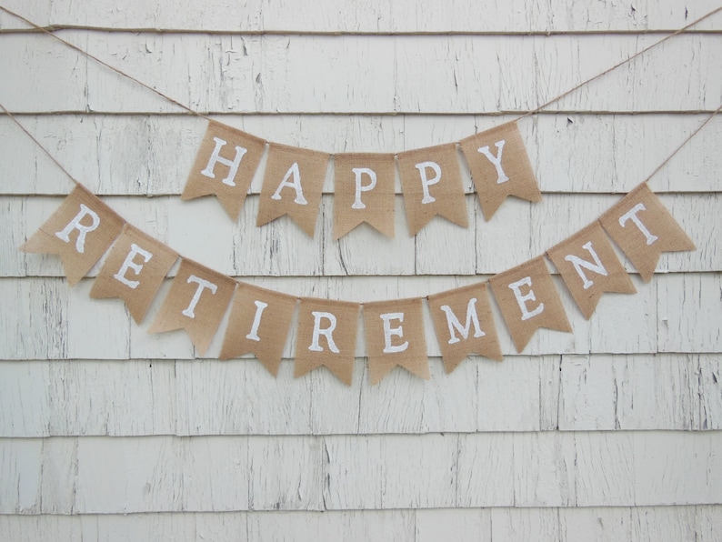 May include: A burlap banner with the words "Happy Retirement" in white letters. The banner is strung on a white wooden wall.