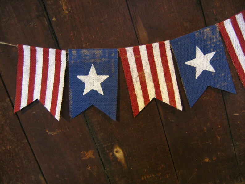 May include: A bunting banner with red, white, and blue fabric flags. The flags have a star design and stripes. The banner is hanging on a wooden surface.