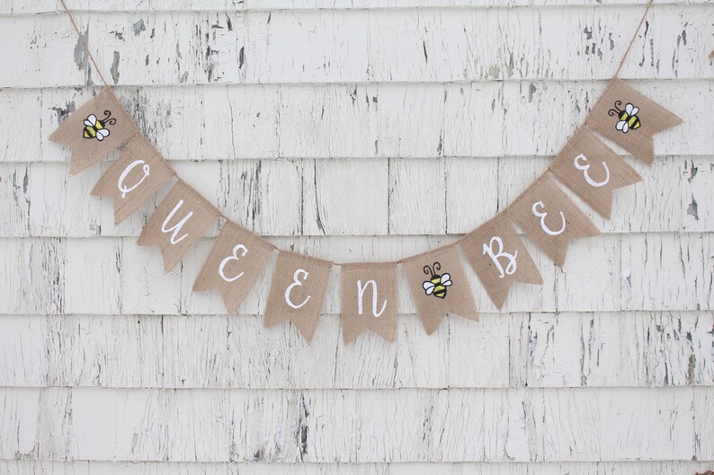 May include: A burlap banner with the words "Queen Bee" in white lettering. The banner is decorated with small bee illustrations.