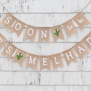 May include: A burlap banner with the text "Mrs. to be" and "Soon Melhado" with a cactus graphic on each banner.