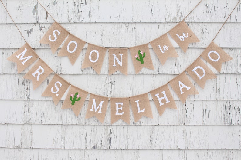 May include: A burlap banner with the text "Mrs. to be" and "Soon Melhado" with a cactus graphic on each banner.
