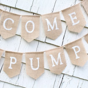 May include: A burlap banner with the words "Welcome Pumpkin" in white paint. The banner is decorated with small orange pumpkins.