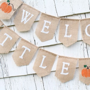 May include: A burlap banner with the words "Welcome Little Pumpkin" in white paint. The banner is strung with twine and features a small pumpkin graphic on each end.