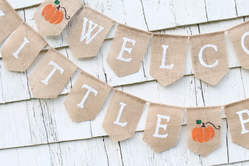 May include: A burlap banner with the words "Welcome Little Pumpkin" in white paint. The banner is strung with twine and features a small pumpkin graphic on each end.