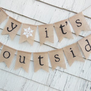 May include: A burlap banner with the text "Baby it's outside" in black lettering. The banner has white snowflake accents.