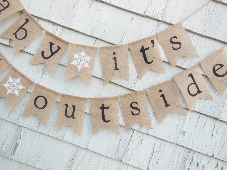 May include: A burlap banner with the text "Baby it's outside" in black lettering. The banner has white snowflake accents.