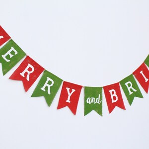 May include: A festive banner with red and green pennants spelling "MERRY and BRIGHT" in white letters. The banner is strung on a thin twine, perfect for holiday decorations. The pennants have a textured, burlap-like appearance.