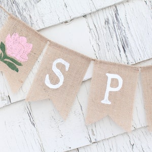 May include: A burlap banner with the word "SPRING" spelled out in white paint. The first flag has a pink flower with green leaves.