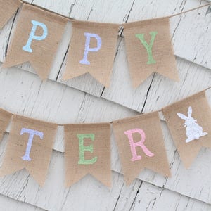 May include: A burlap banner with the words "Happy Easter" in pastel colors. The banner also features a white silhouette of a bunny rabbit.