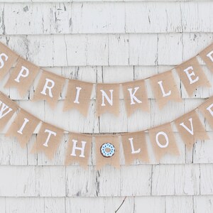 May include: A burlap banner with the text "Sprinkled with Love" in white letters. The banner is decorated with blue and brown donut images.
