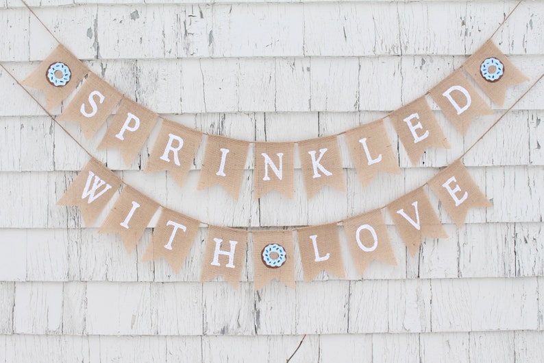 May include: A burlap banner with the text "Sprinkled with Love" in white letters. The banner is decorated with blue and brown donut images.