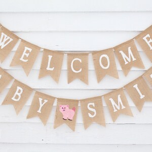 Pode incluir: Uma faixa de serapilheira com as palavras "WELCOME BABY SMITH" em letras brancas. A faixa &eacute; decorada com uma vaca, um porco e um galo. Perfeita para um ch&aacute; de beb&eacute; ou para decorar o quarto do beb&eacute;.