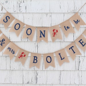 May include: A burlap banner with the text "Mr. & Mrs. Bolter Soon to be" in blue and red lettering. The banner is decorated with a red lobster illustration.