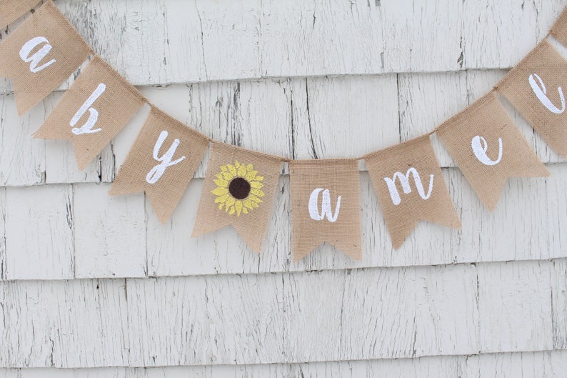 May include: A burlap banner with the words "Welcome" spelled out in white letters. A yellow sunflower is in the center of the banner.