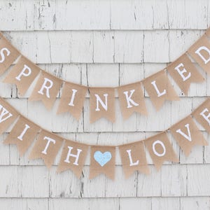 May include: A burlap banner with the text "Sprinkled with Love" in white letters. The banner is decorated with blue hearts.
