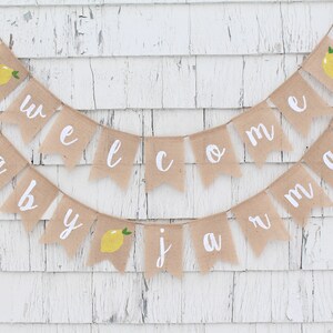 May include: A burlap banner with the words "Welcome Baby" and a lemon design. The banner is strung with twine and has white lettering.
