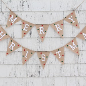 May include: A festive burlap banner spelling out "MERRY CHRISTMAS" in white capital letters. Each triangular flag is adorned with red and green polka dots. The banner is suspended on twine against a white, weathered wooden backdrop.