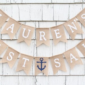 May include: A burlap banner with the text "Lauren's Last Sail" in white letters. The banner is decorated with blue anchor symbols.