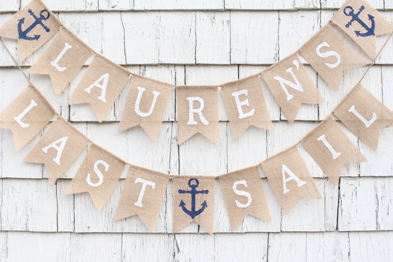 May include: A burlap banner with the text "Lauren's Last Sail" in white letters. The banner is decorated with blue anchor symbols.