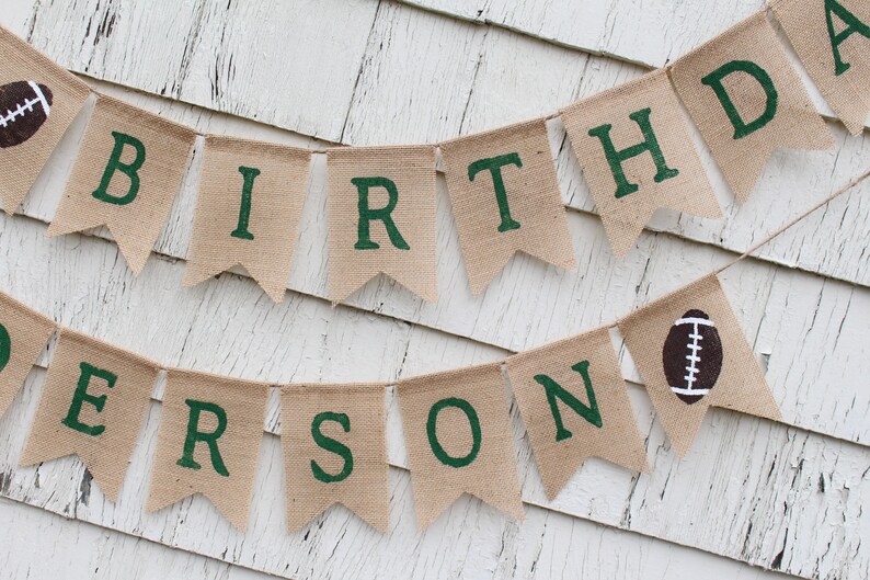 May include: A burlap banner with the words "Birthday" and "Person" in green letters. The banner is decorated with brown footballs.