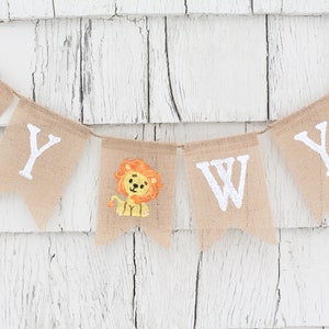 Pode incluir: Uma faixa de juta com as palavras "Baby Wyatt" pintadas de branco. Uma pequena ilustra&ccedil;&atilde;o de le&atilde;o fica entre as palavras "Baby" e "Wyatt".