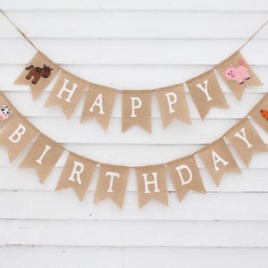 May include: A burlap banner with the words "Happy Birthday" in white letters. The banner is decorated with farm animal illustrations, including a cow, pig, horse, and rooster.