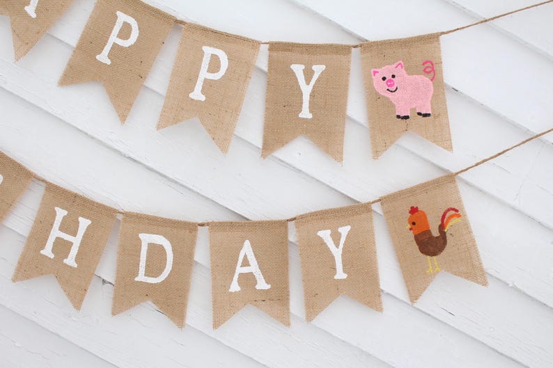 May include: A burlap banner with the words "Happy Birthday" in white letters. The banner is decorated with a pink pig and a brown rooster.