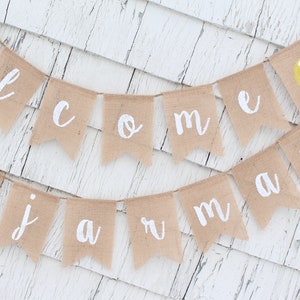 May include: A burlap banner with the words "Welcome to Summer" in white paint. The banner is decorated with small yellow lemons with green leaves.