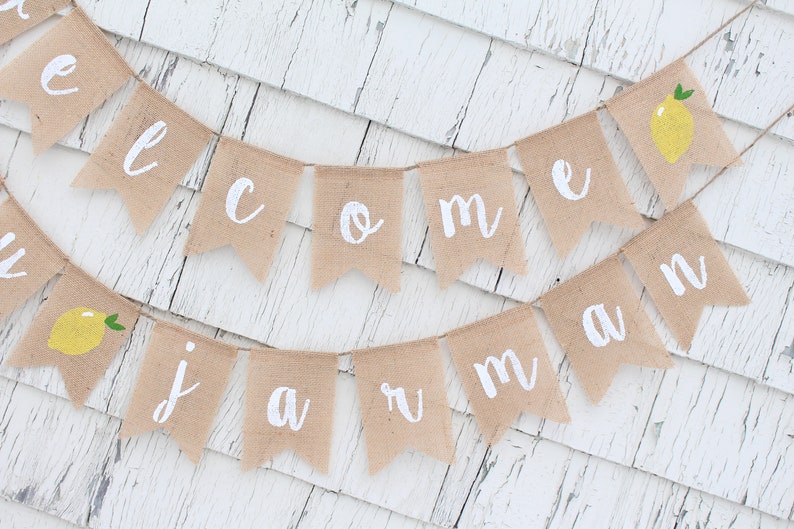 May include: A burlap banner with the words "Welcome to Summer" in white paint. The banner is decorated with small yellow lemons with green leaves.