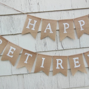 May include: A burlap banner with the words "Happy Retirement" in white letters. The banner is strung up on a white wooden wall.