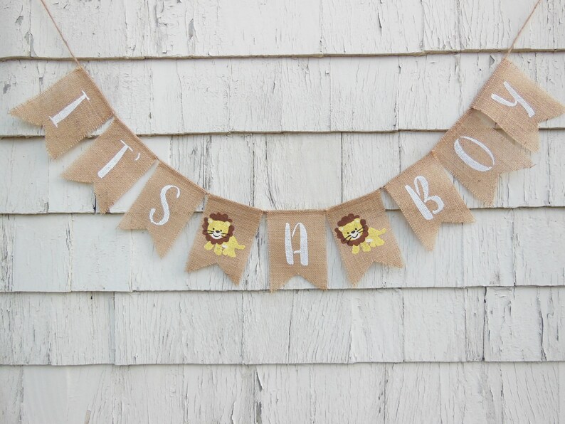May include: A burlap banner with the words "It's a Boy" in white lettering. The banner has small lion illustrations on each of the flags.
