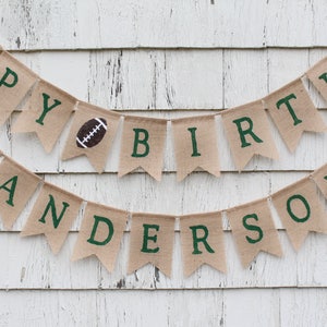 May include: A burlap banner with the words "Happy Birthday Anderson" in green letters. The banner is decorated with brown footballs.