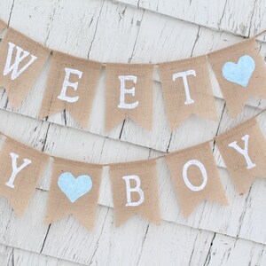 May include: A burlap banner with the words "Sweet Baby Boy" in white paint. The banner has two light blue hearts.