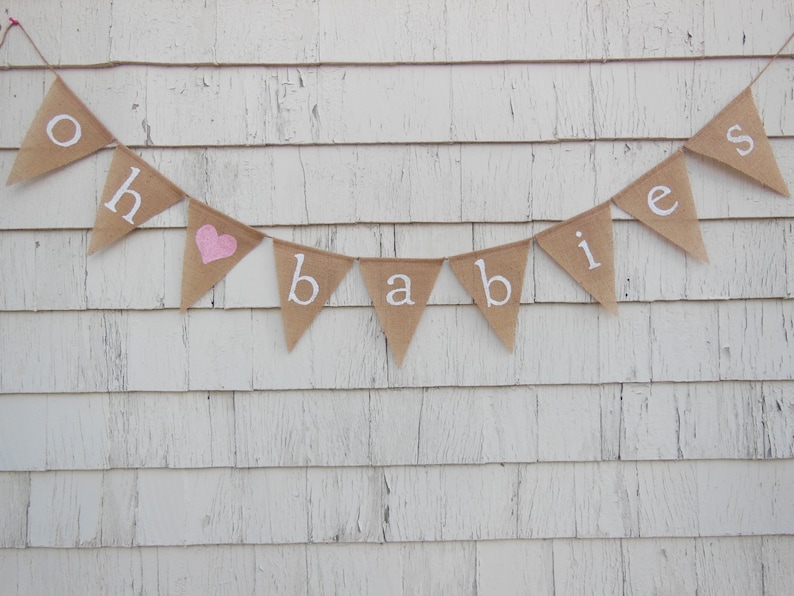 May include: A burlap banner with the words "Oh &hearts; Babies" in white lettering. The heart is pink.